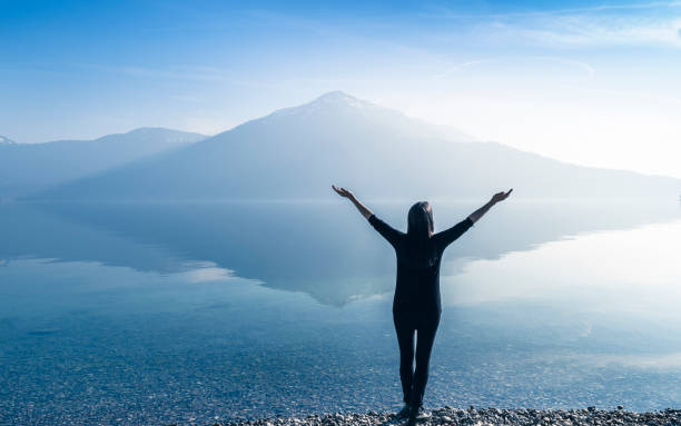 Woman with open arms by the lake on a background of mountains.