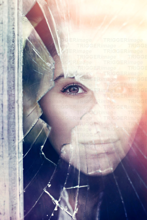 A woman looks through a colourful broken window.